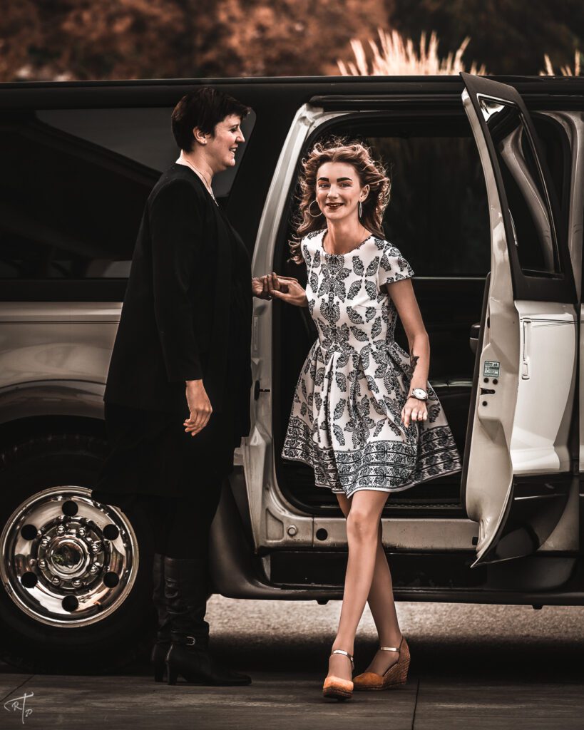 woman in black helping a women in a patterned dress exit an SUV limo
