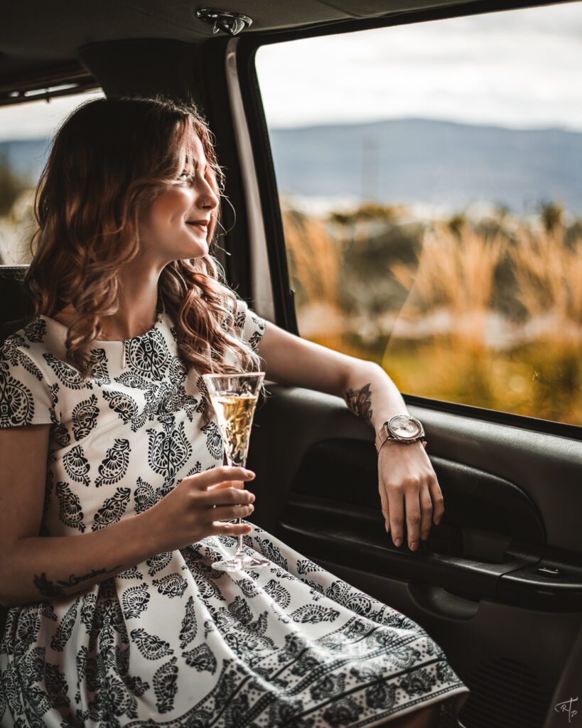 woman dressed up drinking champagne looking out the window of a SUV